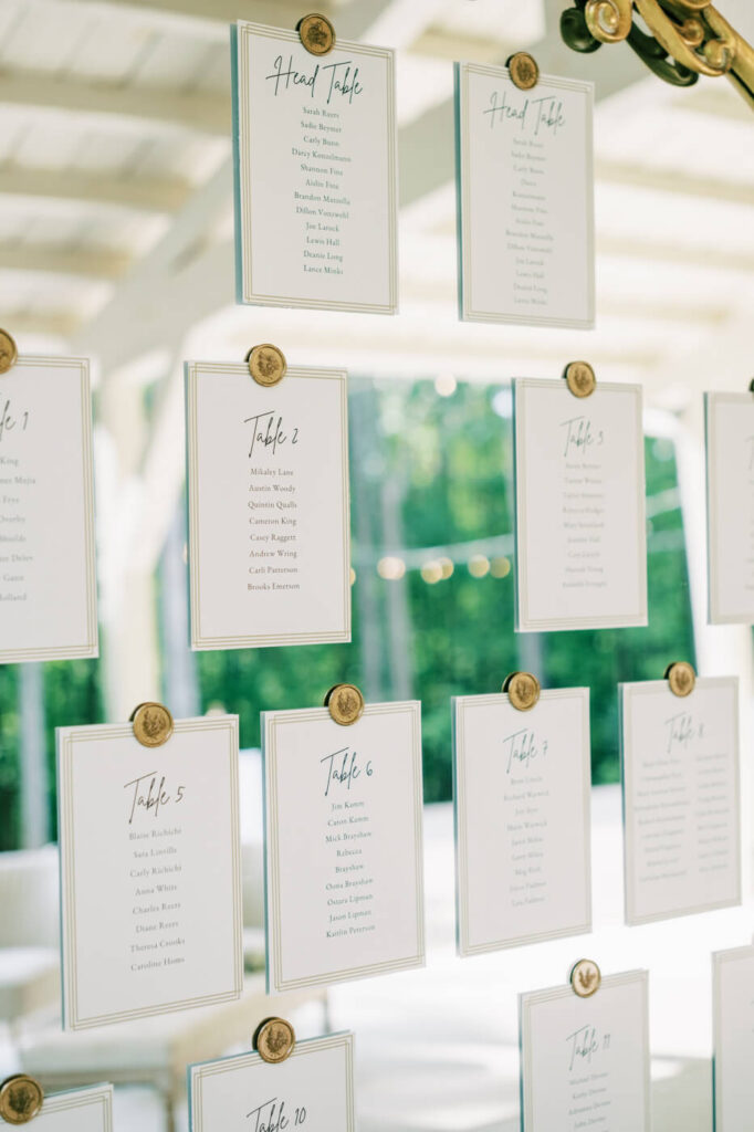 Elegant wedding seating chart display featuring gold wax-sealed cards clipped onto a glass windowpane with soft natural light filtering through.