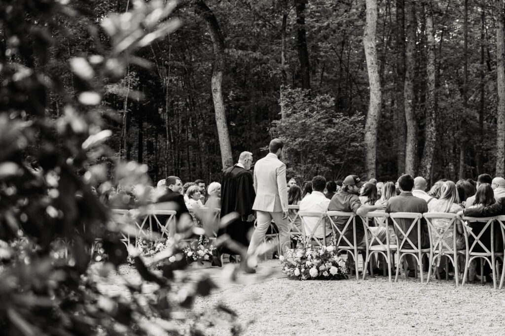 A candid black-and-white shot of the groom looking towards the aisle, waiting for his bride. His emotions are palpable, capturing the significance of this moment.