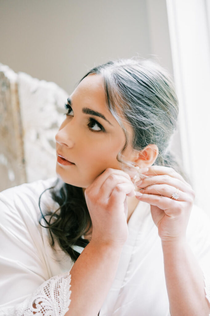 Bride Bonnie putting on her pearl earrings, capturing an intimate bridal prep moment before her Carolina Grove wedding.