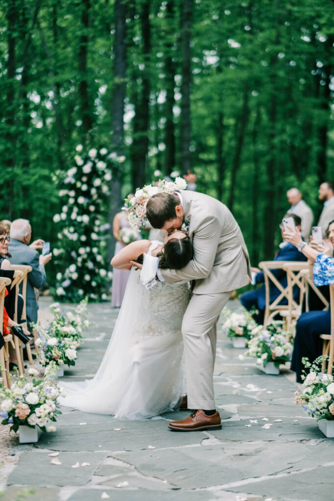 Joyful Dip Kiss – The groom dips the bride in a romantic, celebratory kiss as guests capture the moment with their phones.