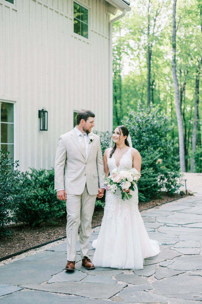 A newlywed couple walks hand in hand outside Carolina Grove, surrounded by lush greenery, sharing a joyful moment on their wedding day.