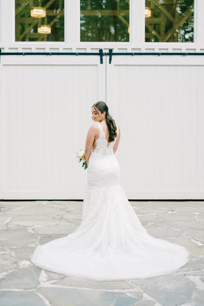 A stunning photo of the bride standing in front of the grand white barn doors, her train elegantly fanned out behind her.