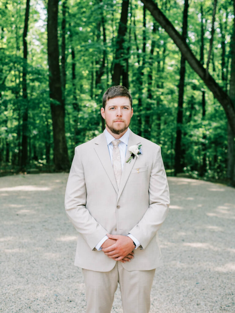 Groom Aiden stands confidently in a light beige suit, awaiting the first look at his Carolina Grove wedding.