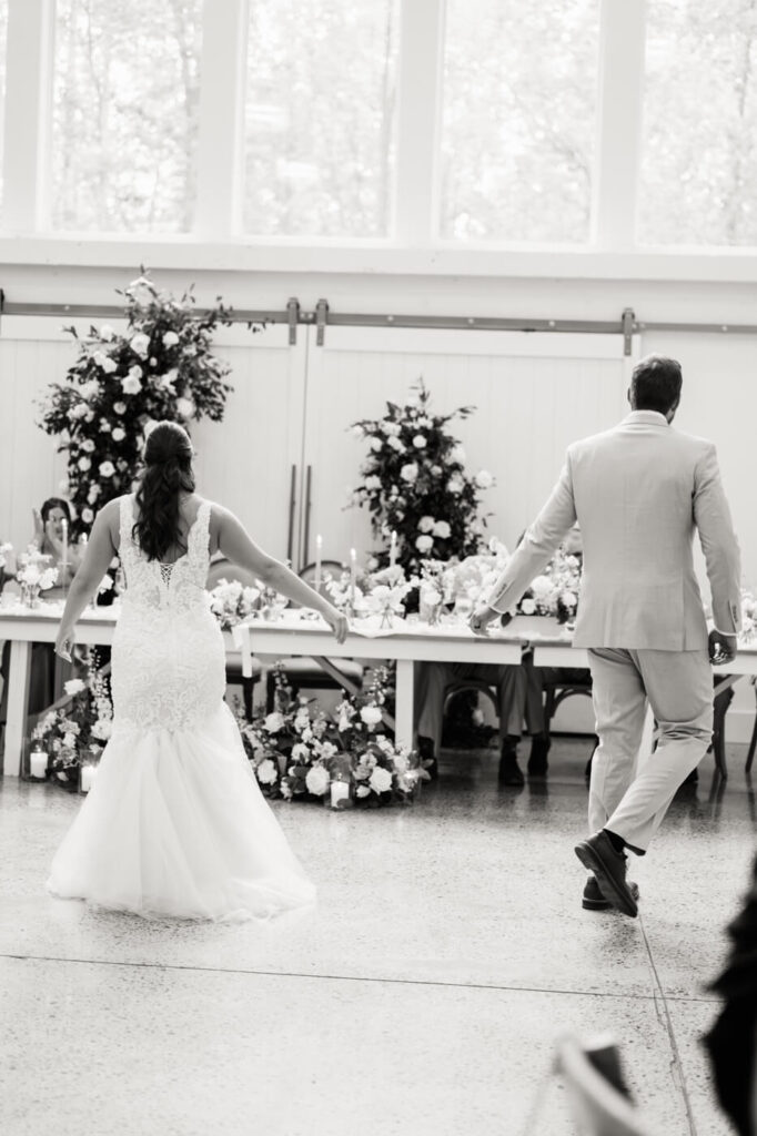 Bride and groom holding hands as they joyfully walk into their reception at Carolina Grove, framed by floral arrangements.