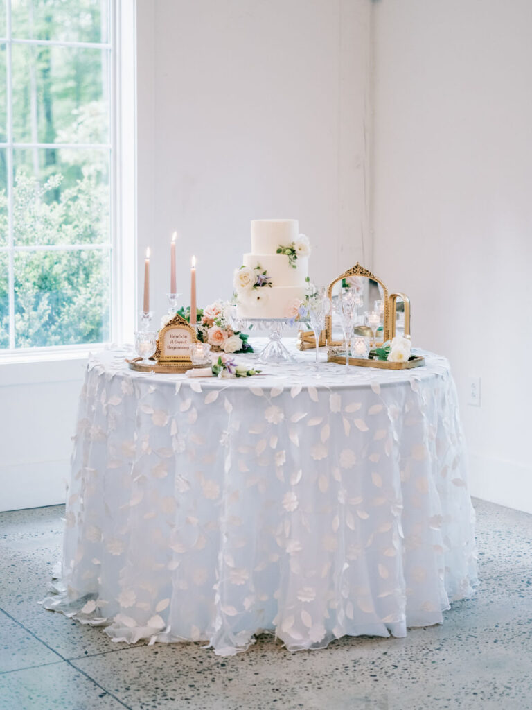 A beautifully styled wedding cake table with soft candlelight, floral accents, and vintage-inspired decor.