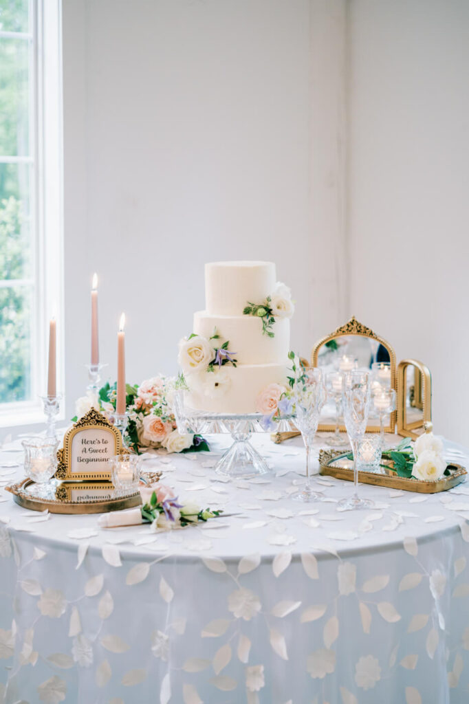 Elegant white wedding cake adorned with blush and ivory flowers, displayed on a romantic reception table.