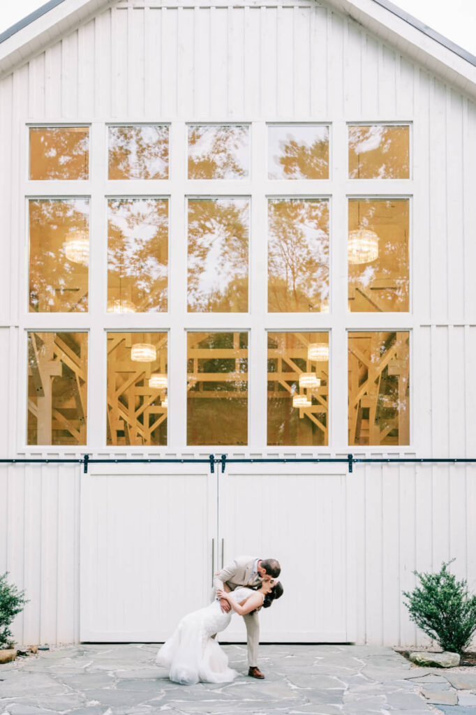 Groom dipping the bride for a romantic kiss in front of the modern barn doors at Carolina Grove.