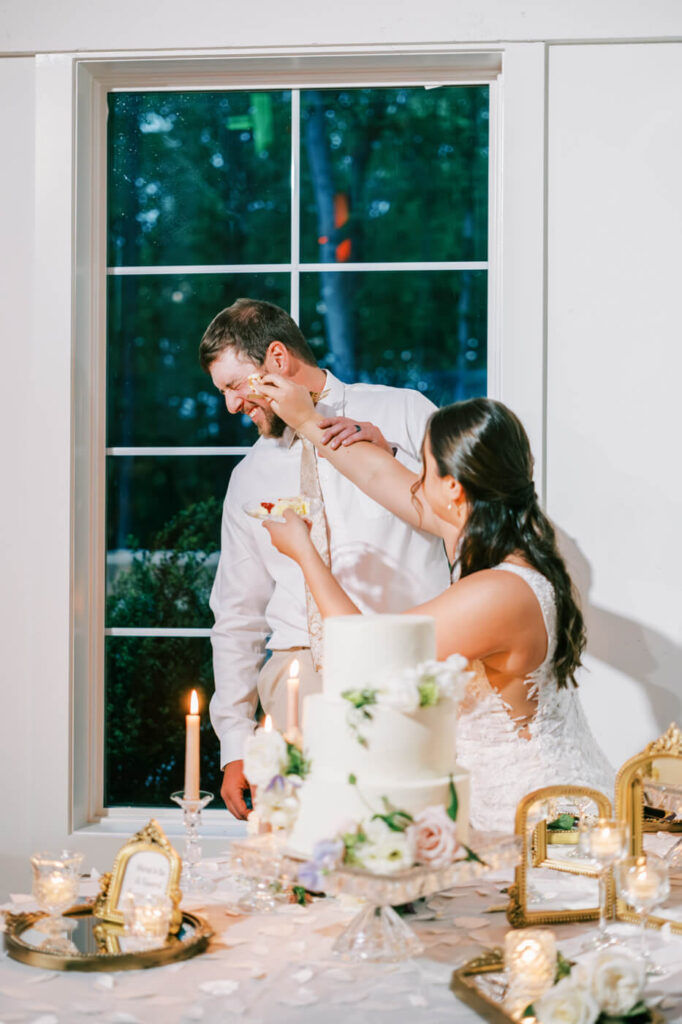 Bride playfully smearing cake on the groom’s face during their wedding cake-cutting celebration.