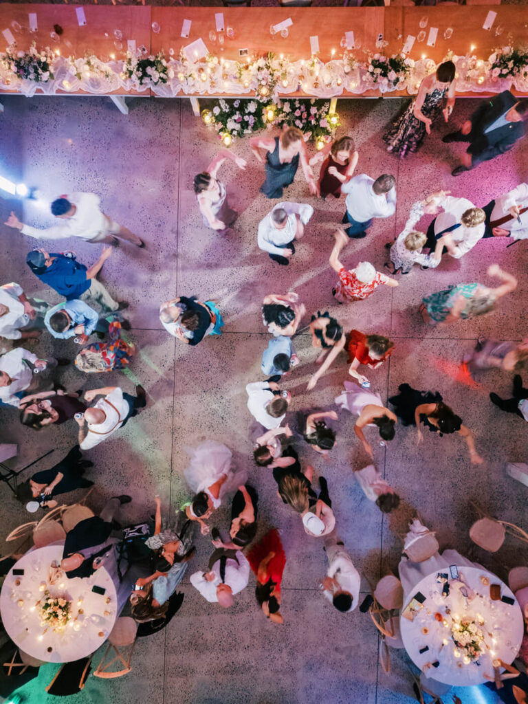 Vibrant wedding dance floor moment – A colorful, energetic top-down shot of guests dancing and celebrating under the warm glow of reception lighting.