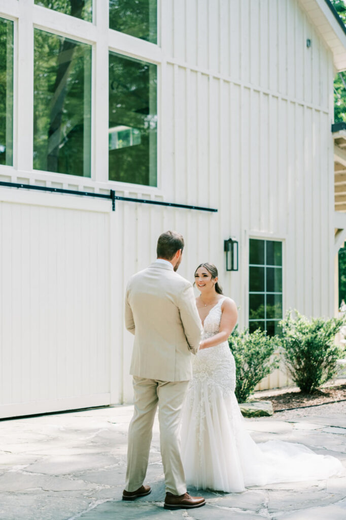 Bonnie & Aiden's emotional first look, sharing a joyful moment outside the elegant white barn at Carolina Grove.