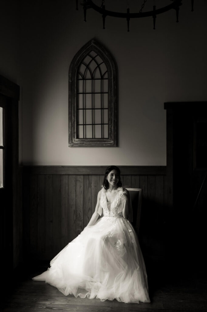 Bride Sitting in Elegant Rustic Room – A black and white bridal portrait of the bride sitting gracefully in a vintage-inspired room at Sweeney Barn, framed by soft natural light.