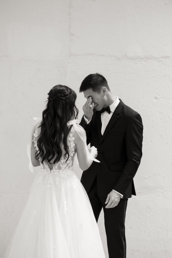 Groom Wiping Away Tears at First Look – A heartfelt black and white photo capturing the groom’s emotional reaction as he sees his bride for the first time.