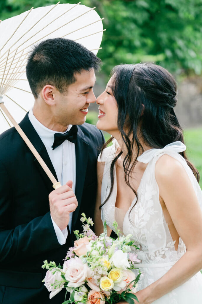 Bride and Groom Laughing with Parasol – A playful and romantic portrait of the bride and groom sharing a joyful moment under a lace parasol, surrounded by lush greenery.