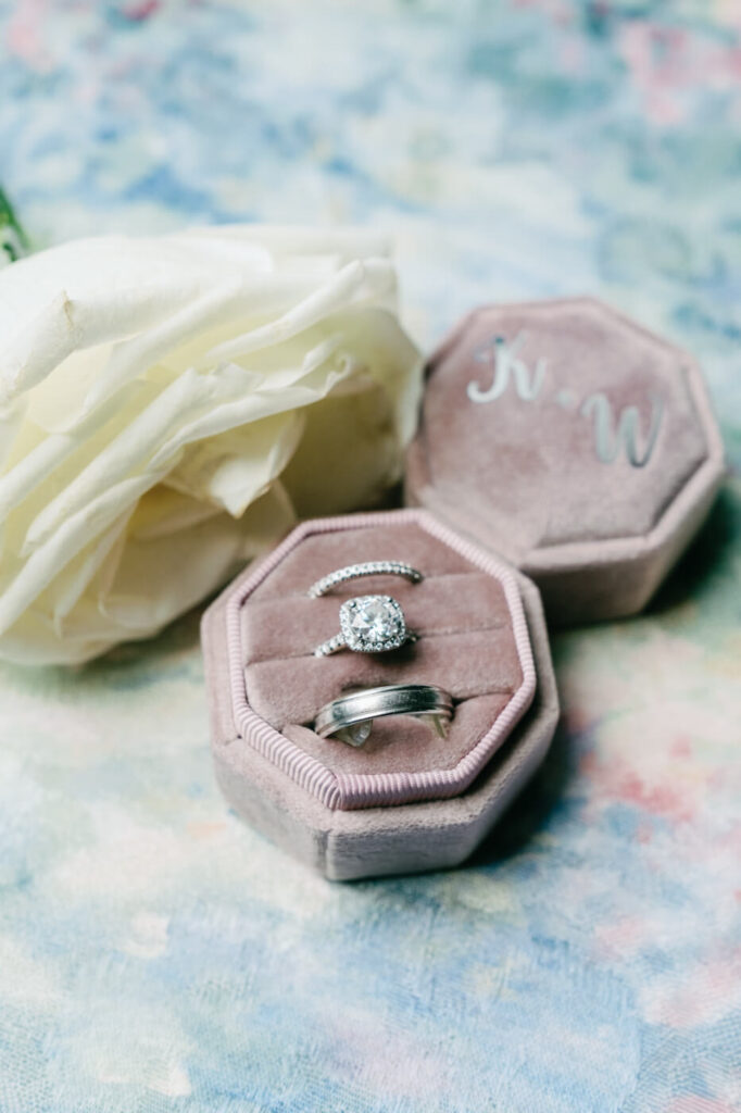 Wedding Rings in Velvet Box – Elegant wedding bands and diamond engagement ring displayed in a personalized velvet ring box with a white rose, capturing the romantic details of a Sweeney Barn wedding.