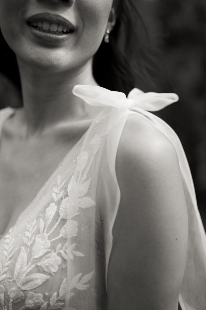 Romantic Close-Up of Bride’s Dress Details – A delicate black and white close-up of the bride’s embroidered floral gown, featuring sheer shoulder bows, taken during their Sweeney Barn wedding.