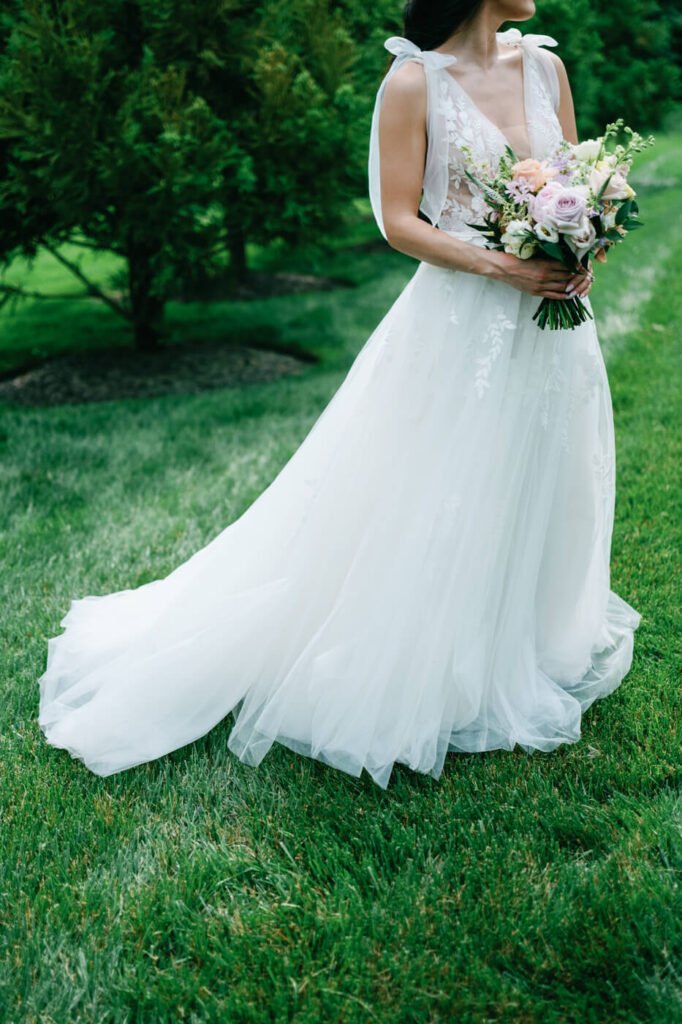 Elegant Bridal Portrait with Flowing Wedding Dress – A close-up shot capturing the bride’s flowing wedding dress and floral bouquet against the vibrant green grass of Sweeney Barn’s scenic grounds.