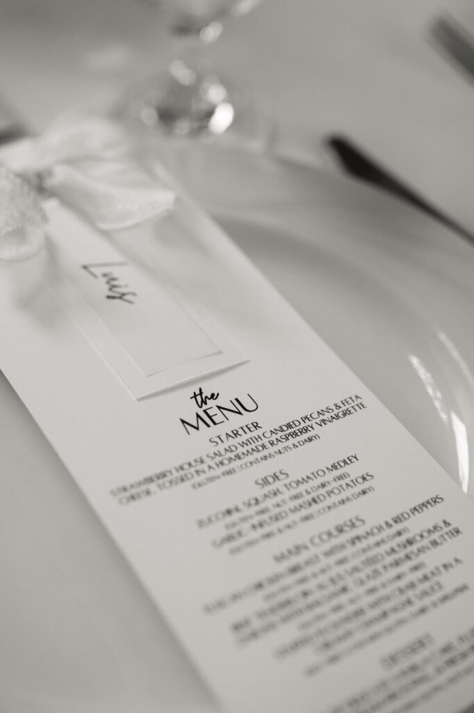 Elegant wedding menu on table – A sophisticated black and white wedding menu with elegant typography sits on a place setting, tied with a delicate white ribbon.