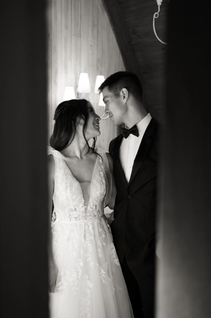 Black and white portrait of bride and groom – The couple shares a dreamy, intimate moment, gazing into each other’s eyes in a softly lit space with glowing wall sconces behind them.