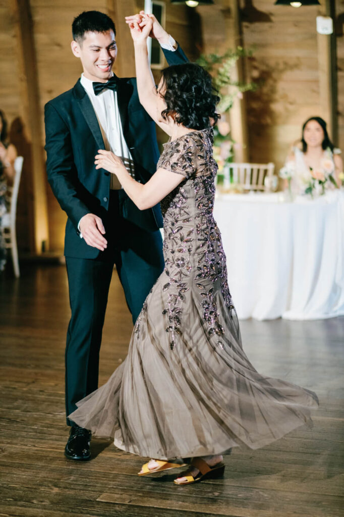 The groom twirls his mother on the dance floor during their mother-son dance, her elegant embroidered gown swirling as they celebrate together.