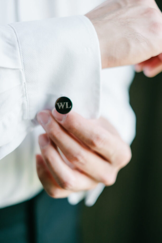 Groom Adjusting Cufflinks – Close-up of groom fastening personalized black cufflinks with his initials, showcasing refined wedding details before the ceremony at Sweeney Barn.