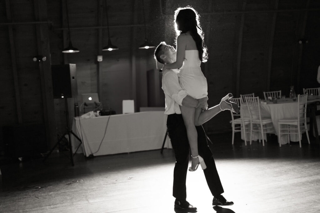 Black and white image of the groom lifting the bride in the air on the dance floor during their private last dance capturing a romantic moment.