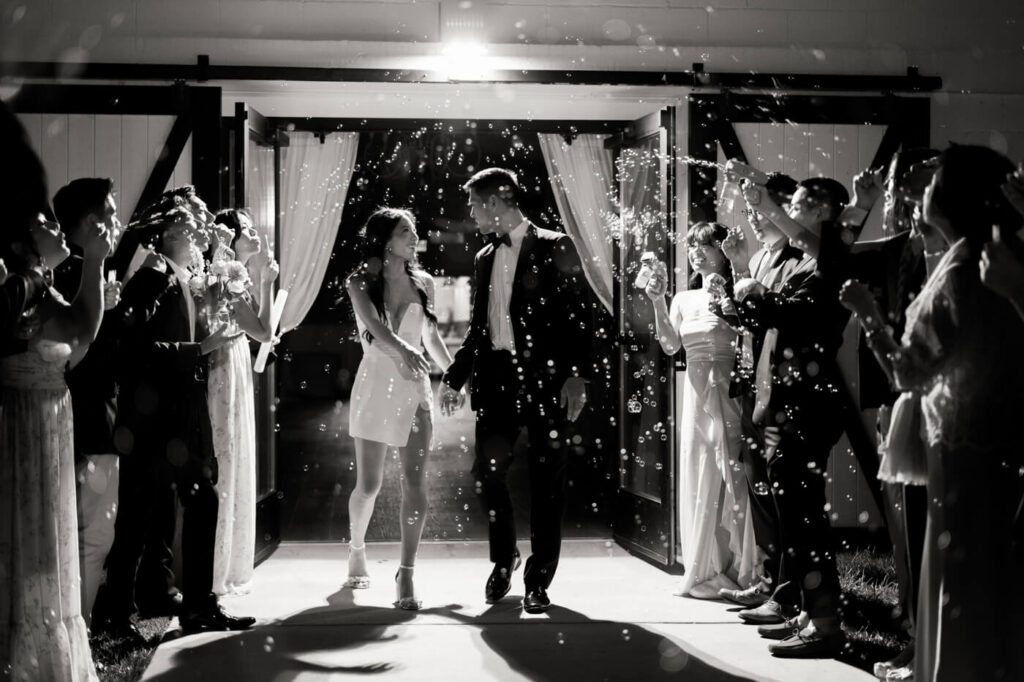 Black and white image of the bride & groom exiting the Sweeney Barn amidst lots of bubbles for their bubble grand exit for a timeless moment.