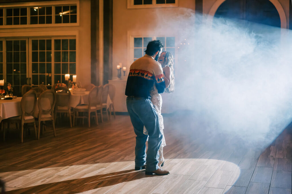 Last dance under romantic wedding reception lights – The groom twirls his bride in a warmly lit barn venue, as soft lighting and wooden beams create a cozy, rustic wedding atmosphere.