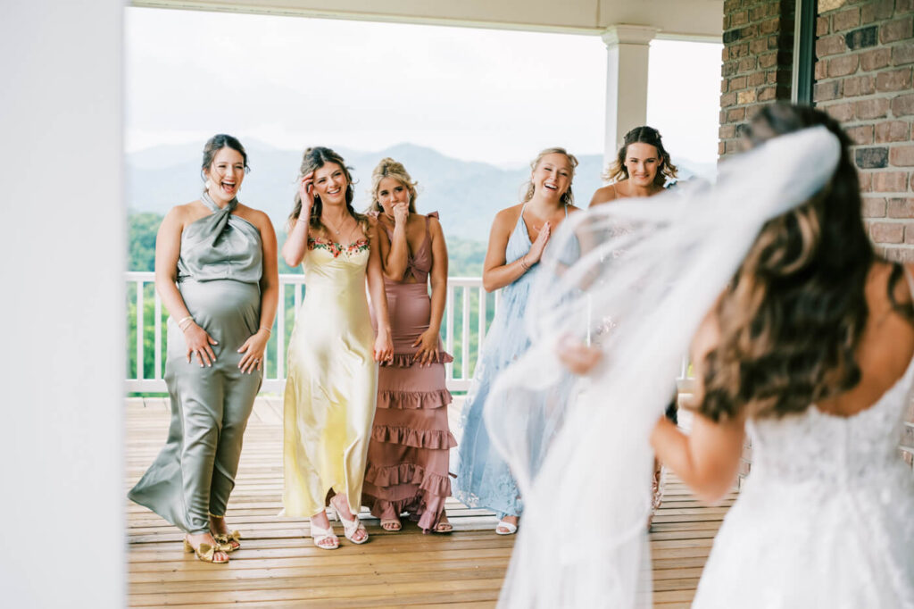 Bridesmaids in pastel dresses reacting to bride during their first look at an Asheville mountain wedding by The Reeses.