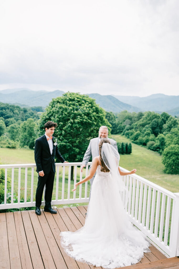 Bride and father sharing a first look on a deck with mountains behind, part of an Asheville mountain wedding by The Reeses.