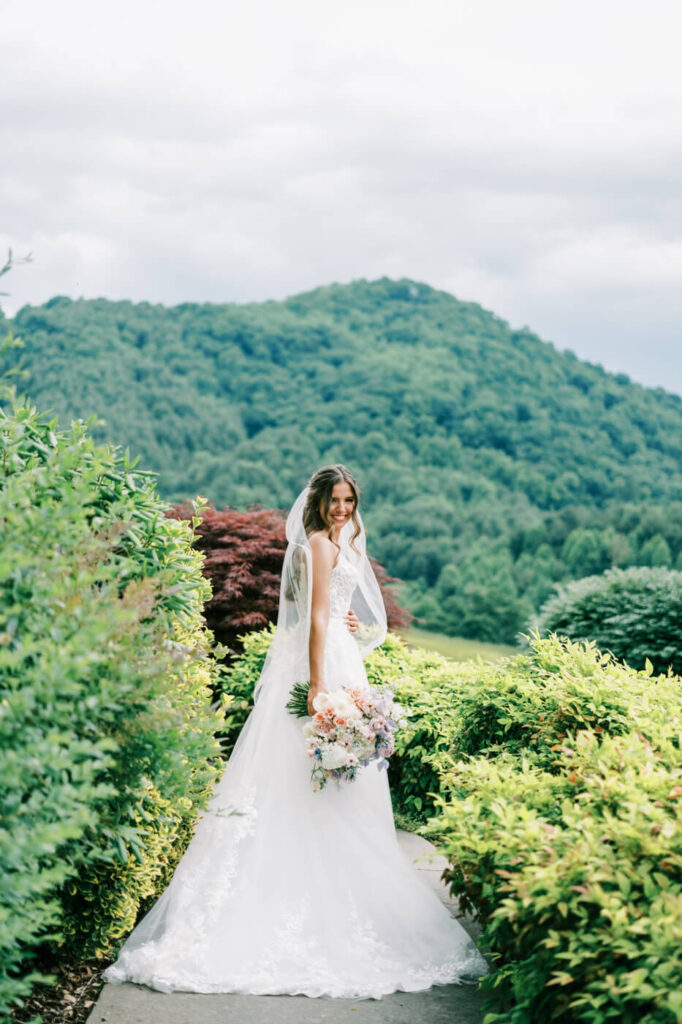 Bride in lace gown with bouquet on a garden path, featured in an Asheville mountain wedding by The Reeses.