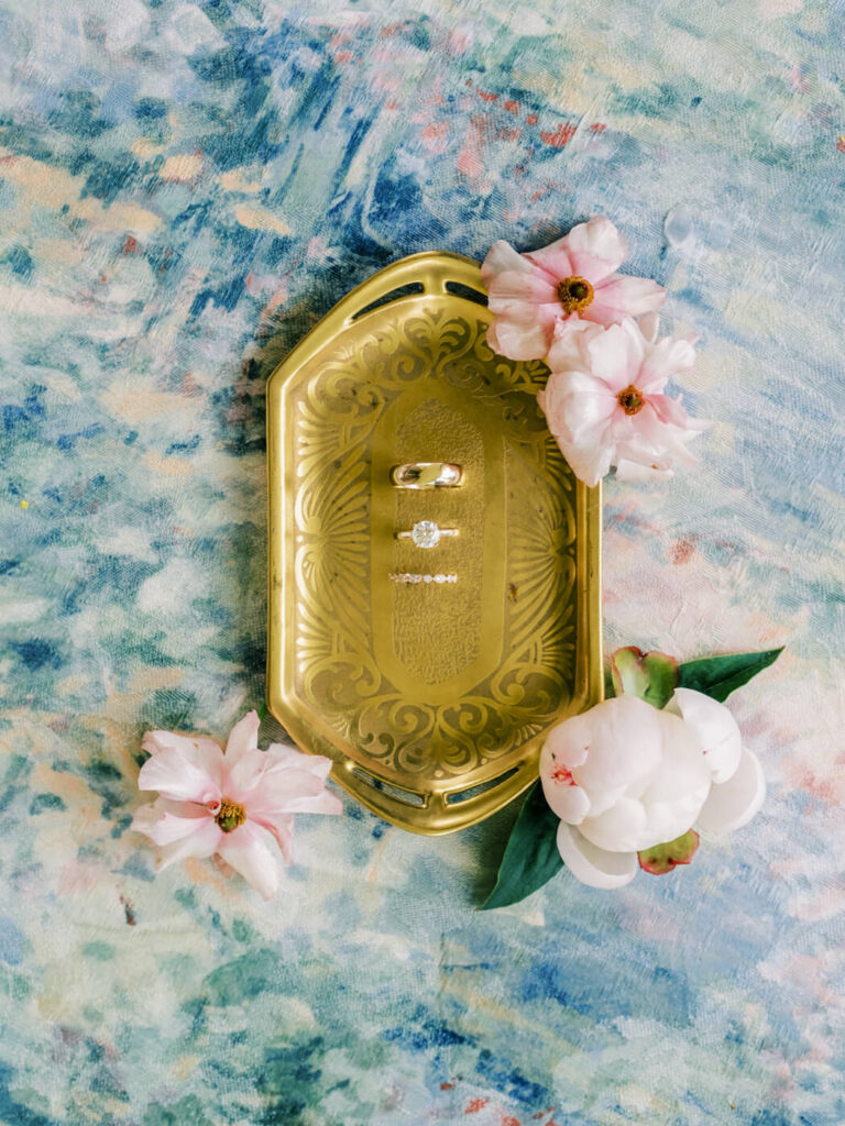 Wedding rings on a gold tray with pastel flowers, detail from an Asheville mountain wedding photographed by The Reeses.