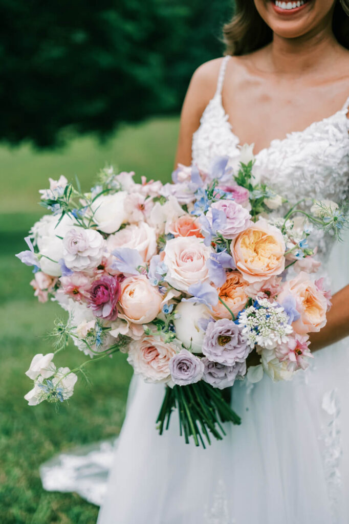 Bride in lace gown holding a colorful bouquet in a field, featured in an Asheville mountain wedding by The Reeses.