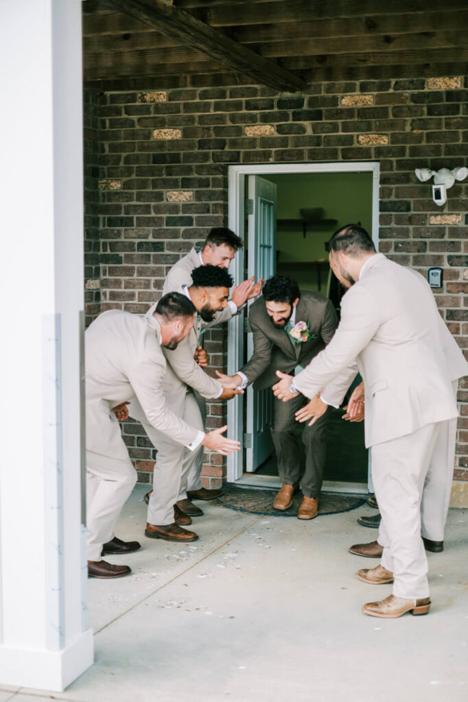 Groomsmen in suits welcoming groom at the door, part of an Asheville mountain wedding photographed by The Reeses.