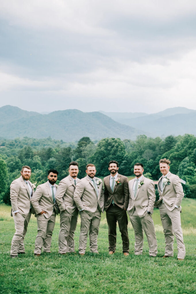 Groomsmen in coordinated suits posing with blue ridge mountains behind, part of an Asheville mountain wedding by The Reeses.