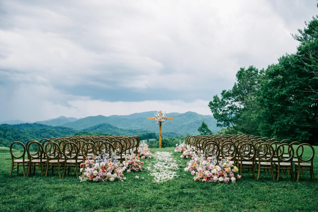 Outdoor ceremony setup with wooden cross and floral arrangements, part of an Asheville mountain wedding by The Reeses."