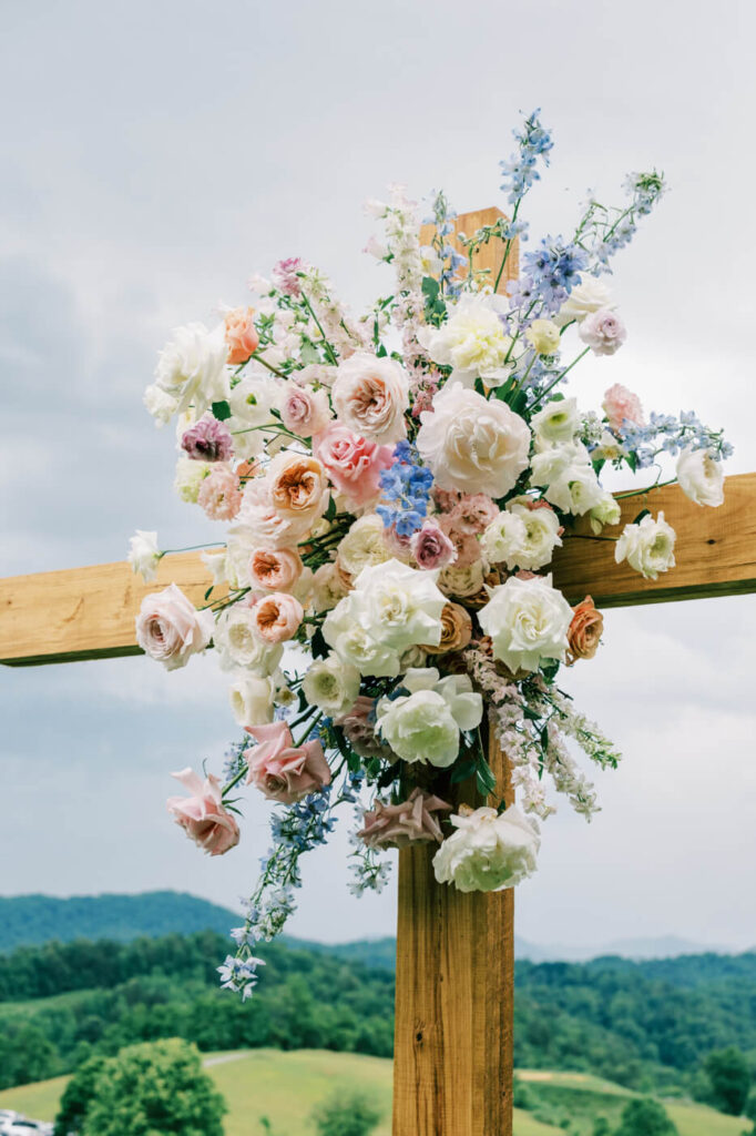 Ceremony setup with floral-decorated cross and mountain backdrop, part of an Asheville mountain wedding by The Reeses.