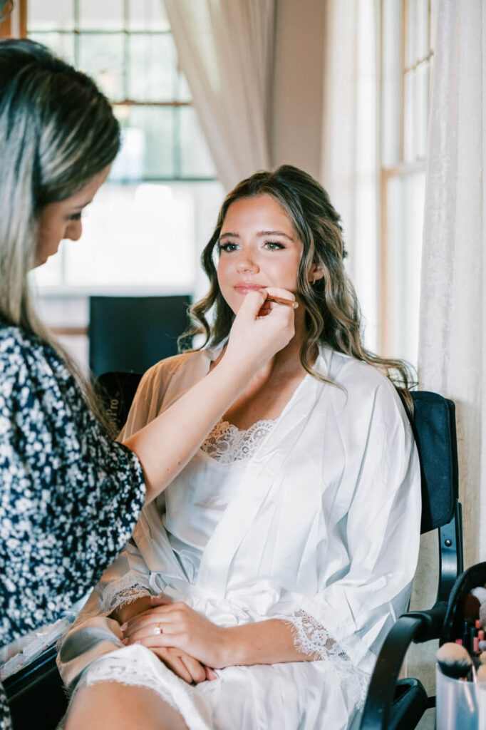 Bride receiving makeup touch-up in a robe, preparing for an Asheville mountain wedding captured by The Reeses.