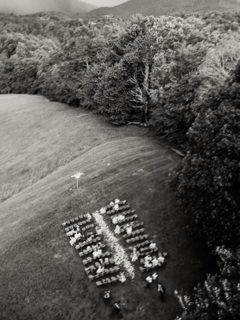 Aerial black and white view of outdoor ceremony with guests running from the rain, part of an Asheville mountain wedding by The Reeses.