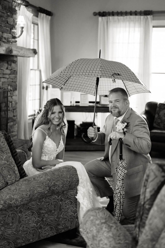 Father holding umbrella over bride in black and white, part of an Asheville mountain wedding photographed by The Reeses.