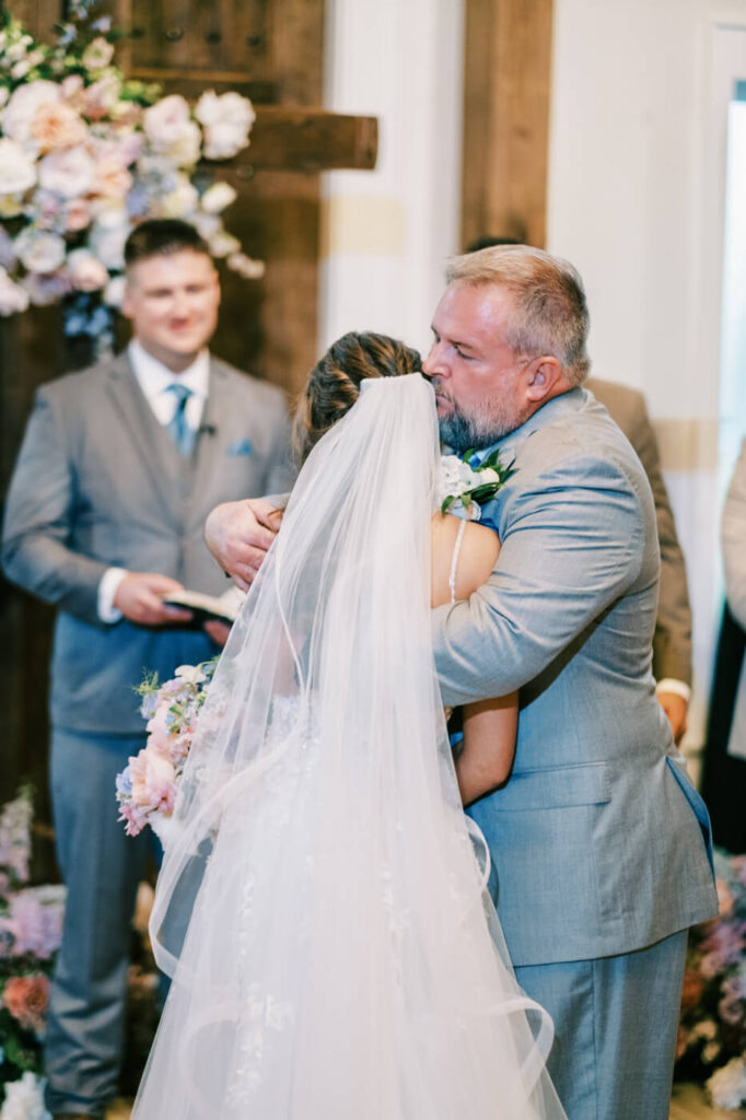 Father hugging bride in lace gown during ceremony, part of an Asheville mountain wedding by The Reeses.