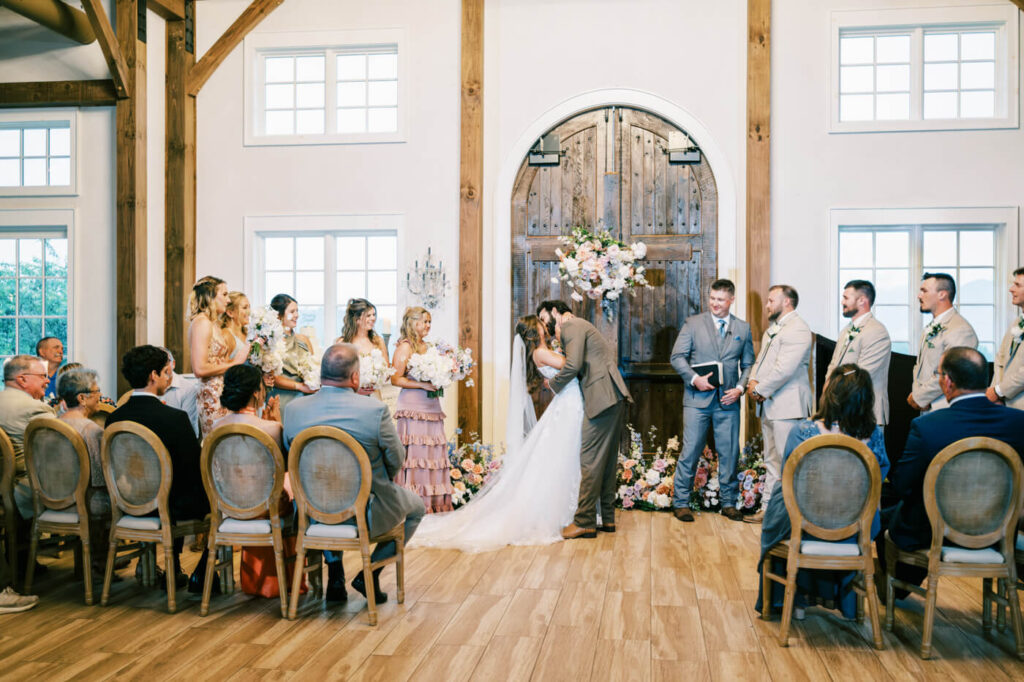 Bride and groom first kiss during indoor ceremony, part of an Asheville mountain wedding by The Reeses.