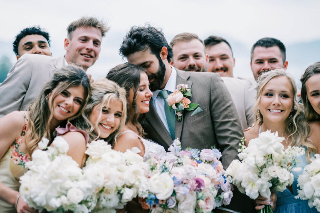 Bride and groom embracing surrounded by their wedding party with bouquet and mountains, part of an Asheville mountain wedding photographed by The Reeses.