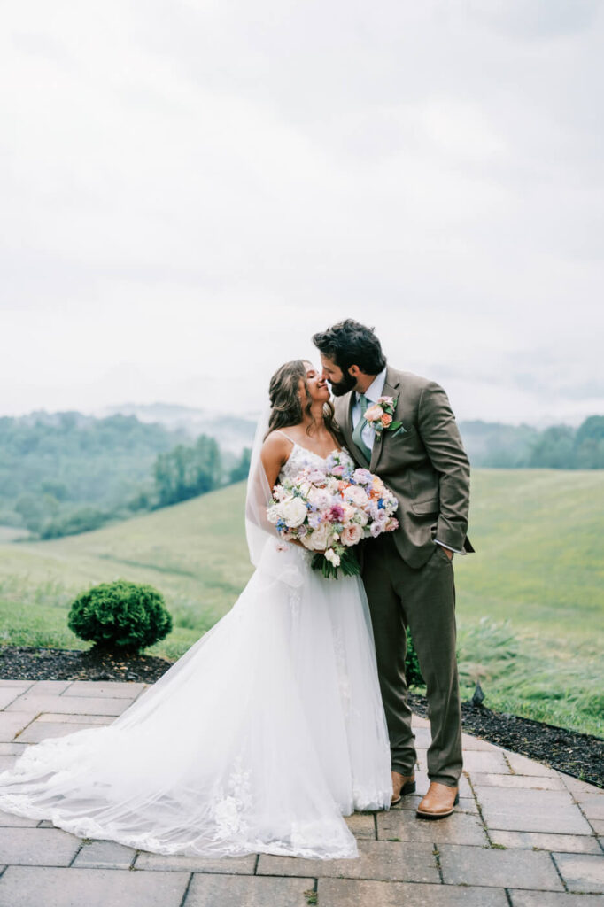 Bride and groom kissing with bouquet outdoors, part of an Asheville mountain wedding captured by The Reeses.