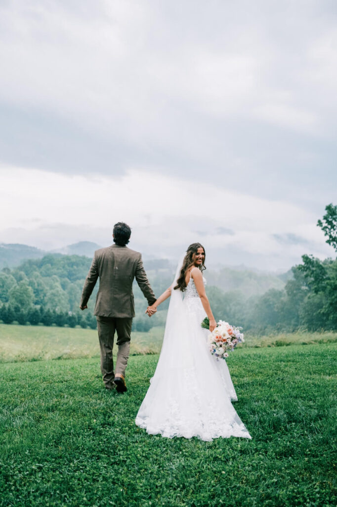 Bride and Groom Walking Hand-in-Hand Through Asheville Mountains – A candid moment as the newlyweds walk away, holding hands, with rolling foggy hills creating a cinematic and romantic atmosphere.