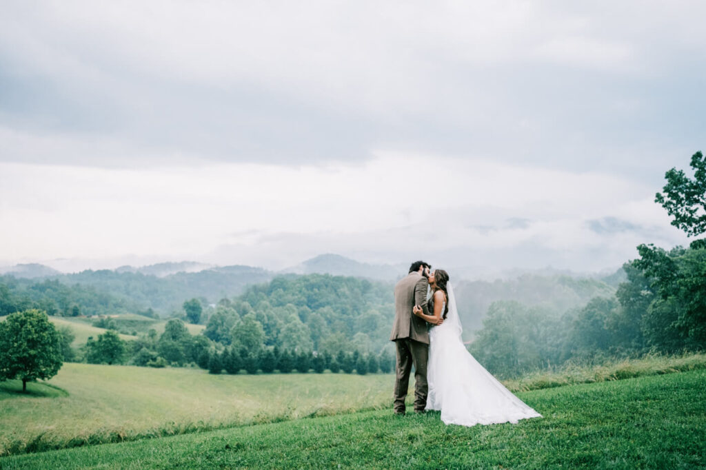 Bride and Groom Kiss in Asheville Mountains – A candid moment as the newlyweds kiss with rolling foggy hills creating a cinematic and romantic atmosphere.