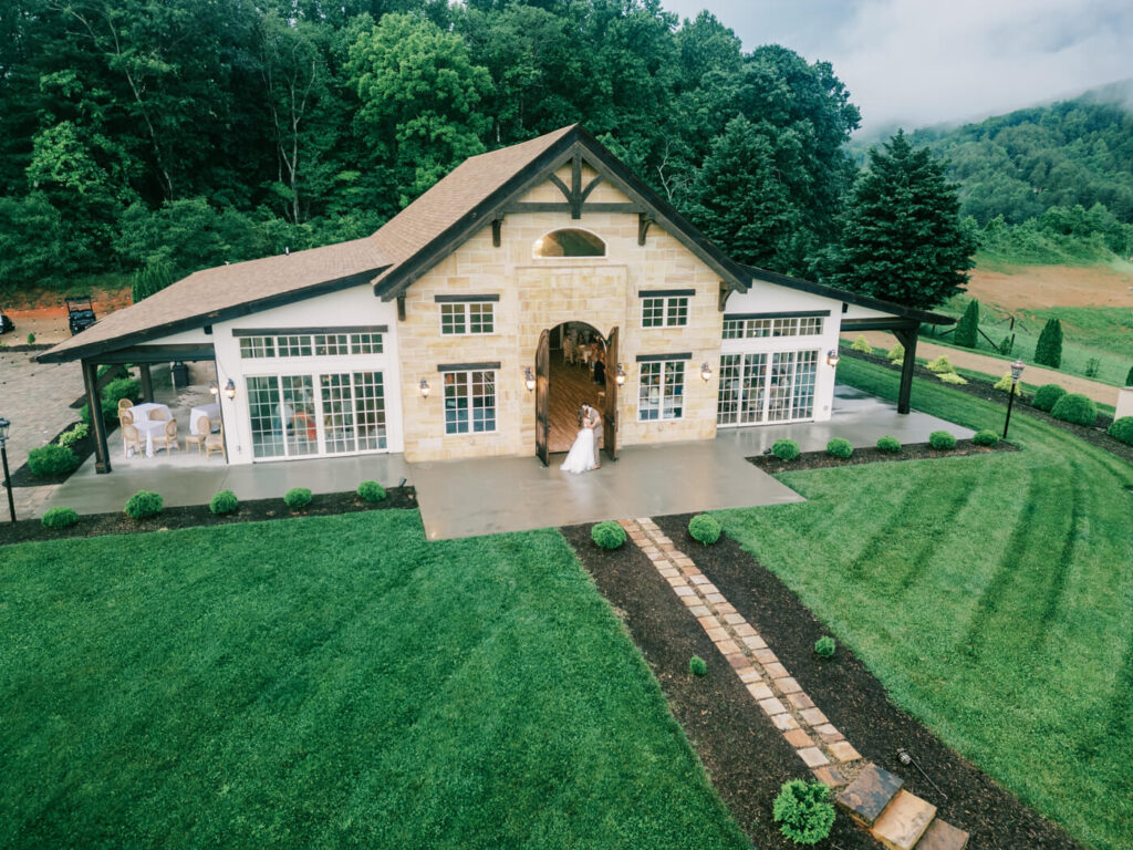 Elegant Outdoor Wedding Venue in Asheville, NC – A stunning aerial view of an elegant mountain wedding venue, surrounded by lush greenery, with the bride and groom framed in the grand entrance.