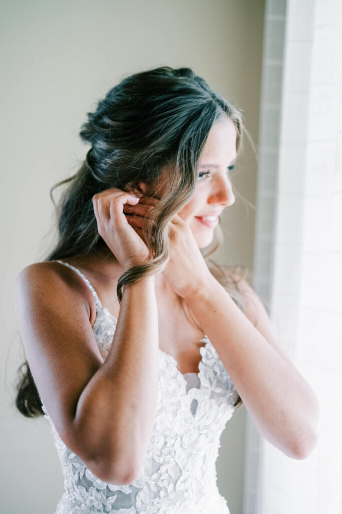 Bride in a lace wedding gown adjusting her earring, preparing for an Asheville mountain wedding captured by The Reeses.