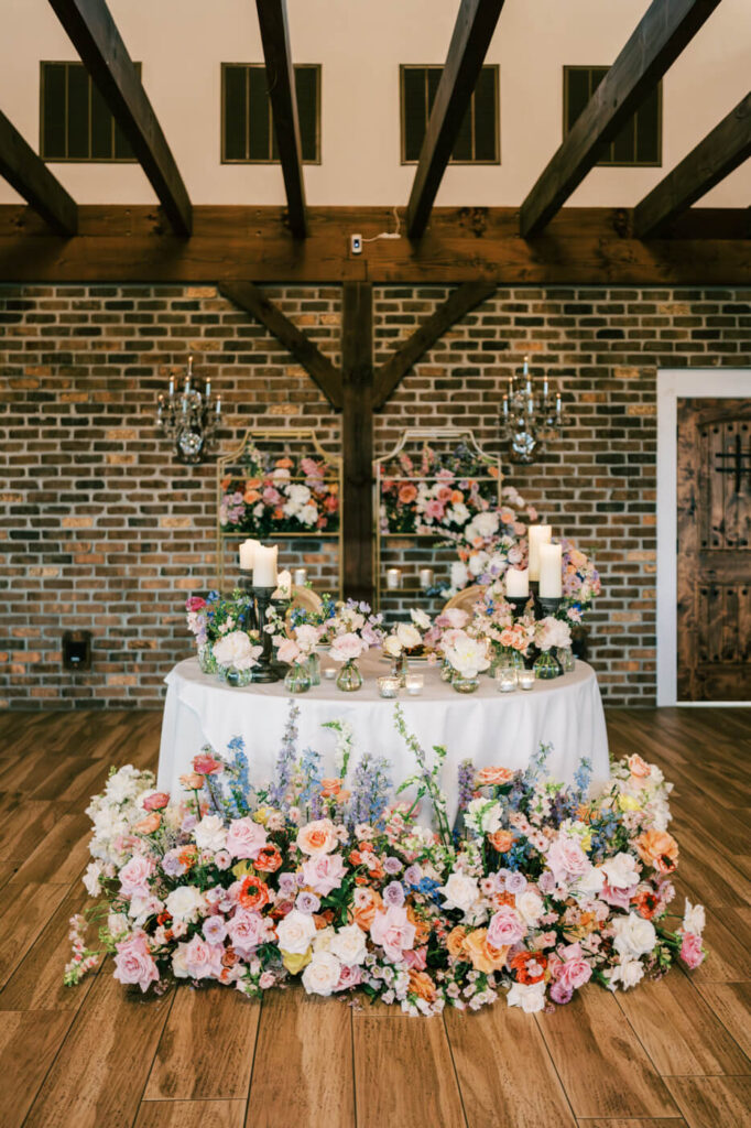 Romantic Asheville Mountain Wedding Reception Table – A beautifully decorated sweetheart table with pastel floral arrangements, candlelit accents, and a rustic brick backdrop at an Asheville mountain wedding.