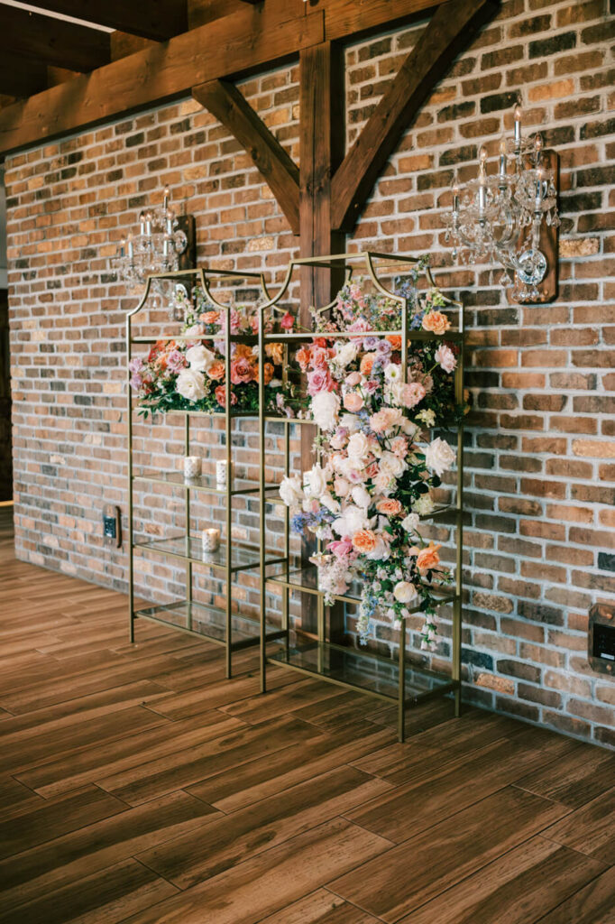 Elegant Floral Display at Asheville Wedding Venue – A gold-framed floral installation with lush pink, peach, and white roses against a rustic brick wall, adding charm to the wedding reception space.