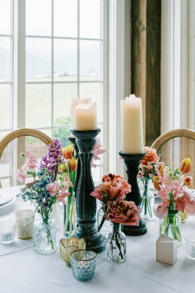 Intimate Wedding Table Setting with Candles and Flowers – A romantic wedding table setting featuring candlelit centerpieces, delicate tulips, roses, and hydrangeas in a light-filled venue with mountain views.